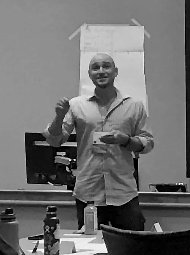 Jesse Jonesberg smiling and gesturing while leading a training session, with participants seated at tables.