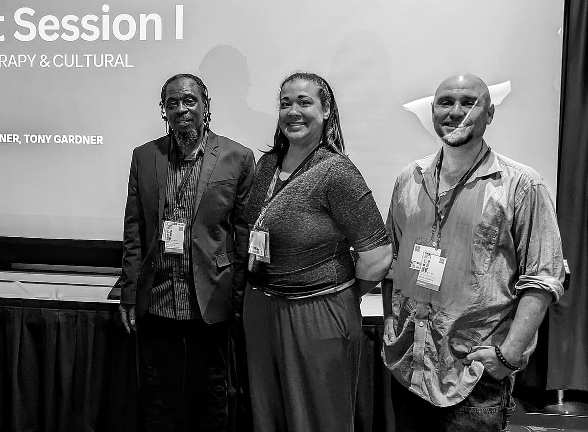 Tony Gardner, Shaina Buckner and Jesse Jonesberg smiling in front of a screen that reads Breakout Session I: Neuroaffirming Therapy and Cultural Humility.