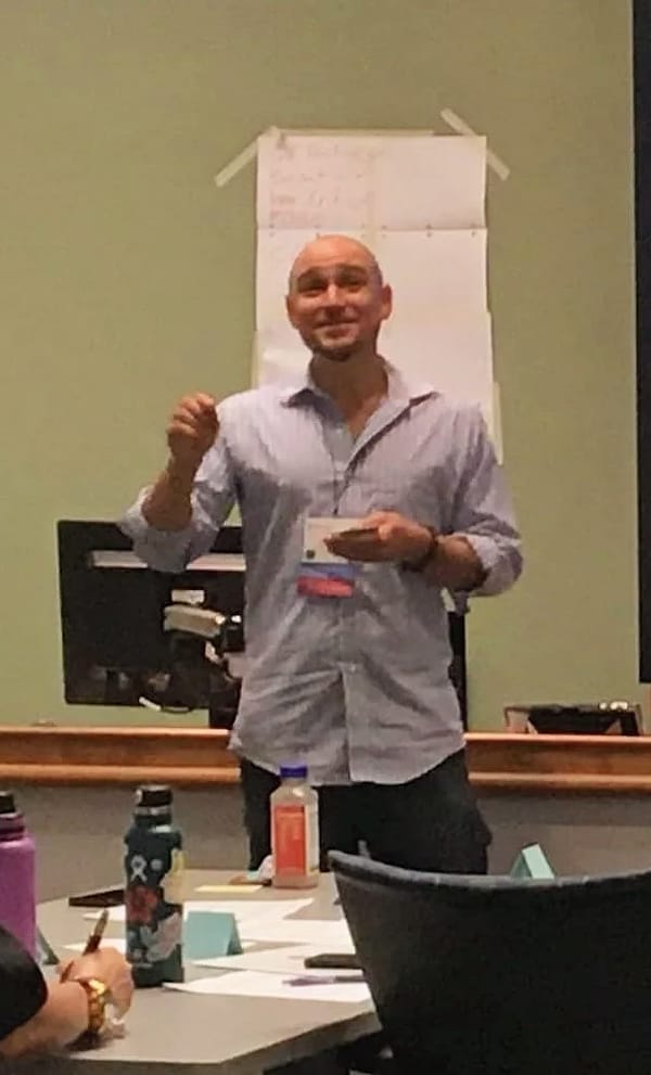 Jesse Jonesberg smiling and gesturing while leading a training session, with participants seated at tables.